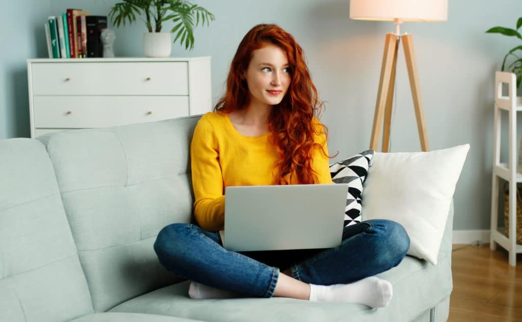 Red haired girl sits on her couch with a laptop