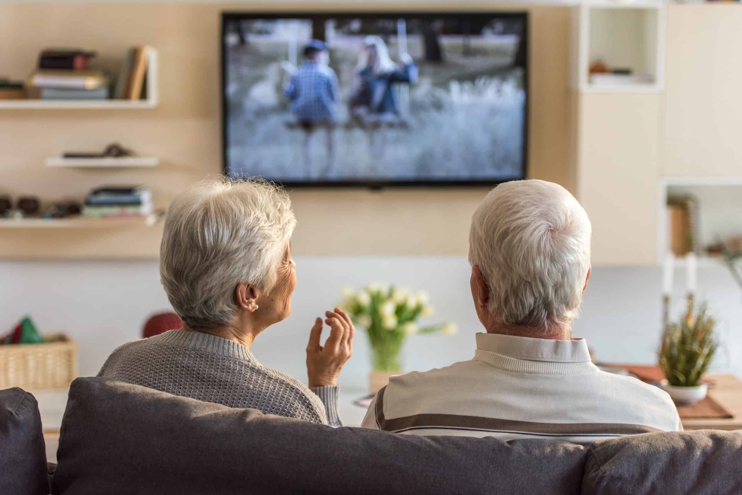 Senior couple sitting on sofa and watching television show at home.