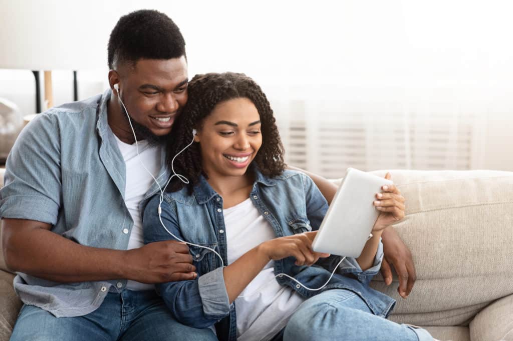 A man and woman share headphones while looking at a tablet